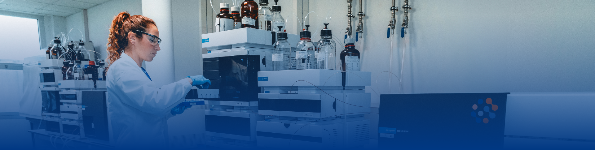 Close up of a scientist wearing a lab coat and protective glasses in a laboratory. She is conducting sterile and non-sterile microbiology testing working with a vial.