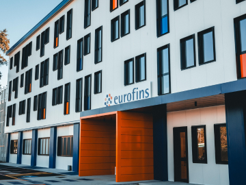 Facade of the Eurofins building, featuring its primary colours of orange and blue, with a prominent entrance and numerous windows. The design emphasizes a modern and professional architectural style, reflecting the company's innovative and dynamic approach