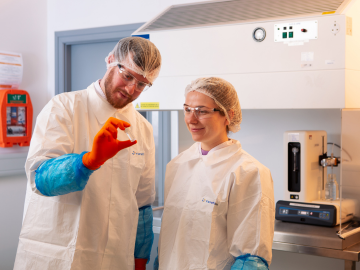 Two scientists in a Eurofins laboratory wearing laboratory coats and protective goggles and holding a vial for particle testing. 