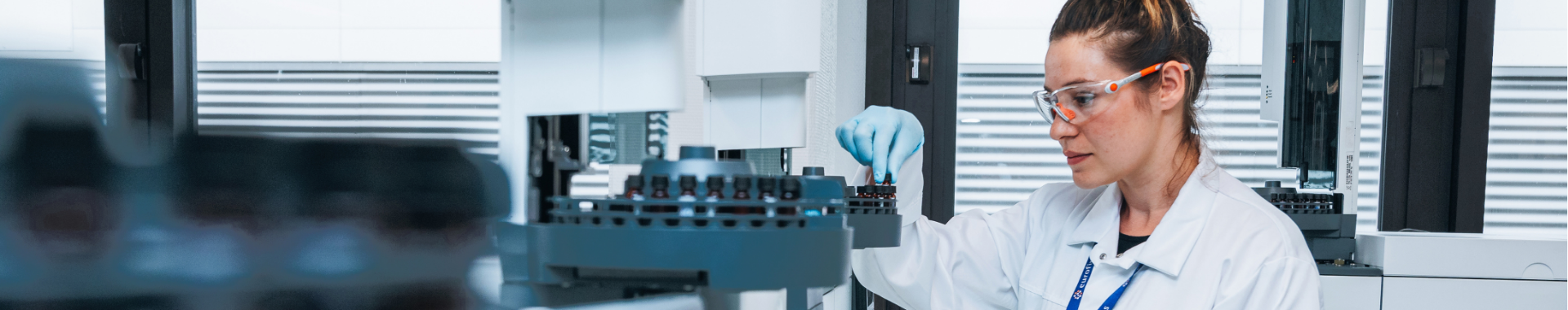 Scientist wearing a lab coat and protective goggles, placing vials in an advanced machine  conducting  Karl Fisher titration. The laboratory is equipped, illustrating the precision of moisture analysis in a professional scientific setting.