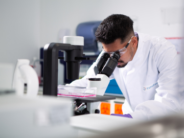 A scientist in a Eurofins laboratory wearing a laboratory coat and protective goggles, he is conducting raw material analysis, looking through a microscope.